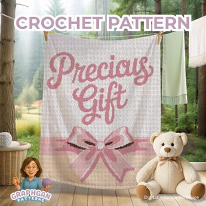 Könnte beinhalten: Eine weiße Häkeldecke mit den Worten "Precious Gift" in Rosa und einem rosa Schleifendesign. Die Decke hängt an einer Wäscheleine. Ein Teddybär sitzt auf dem Boden. Oben steht der Text "CROCHET PATTERN".