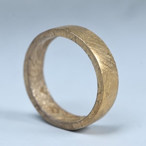 May include: A gold-coloured ring with a textured surface. The ring has a flat band design and a slightly worn appearance. The ring is likely made of metal and is suitable for everyday wear.