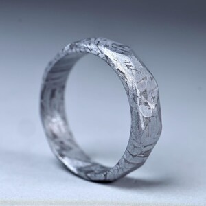 May include: A silver ring with a textured, hammered finish. The ring features an irregular, faceted design, giving it a unique, handcrafted appearance. The metal has a slightly rough surface, adding to its rustic charm. The ring is a piece of jewellery.