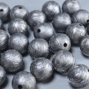 May include: A collection of spherical beads with a dark gray, metallic finish. Each bead features a textured, weathered surface with visible striations and a single centered hole for threading, creating a uniform appearance across the group.