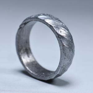 Peut inclure: Une bague argentée texturée avec une surface irrégulière unique. Le design de la bague présente une série de facettes et un anneau légèrement irrégulier, créant une apparence distinctive et artisanale. La bague est une prise de vue rapprochée sur un fond clair.