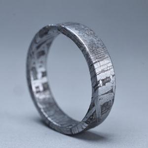 May include: A textured, silver-colored ring with a unique pattern. The ring's surface displays a detailed, layered design, creating a distinctive appearance. The ring is a band style, suitable for everyday wear.