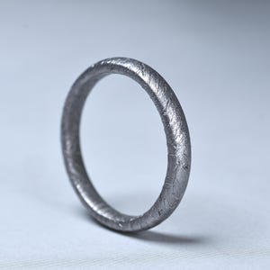 Peut inclure: Une bague argentée à la surface texturée. La bague est circulaire et semble être en métal. La bague est de conception simple, adaptée au quotidien. La bague est présentée sur un fond clair. Le diamètre de la bague est d'environ 2 cm.
