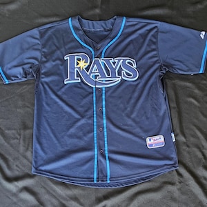 May include: Navy blue baseball jersey with the word "RAYS" in white and light blue across the chest. The jersey has a button-up front, light blue trim, and a team logo patch on the lower right.