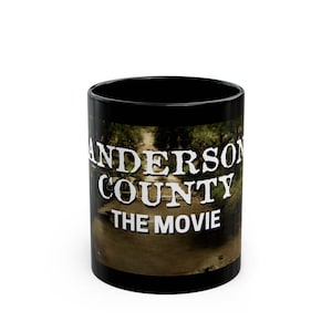 May include: Black ceramic coffee mug with the text "ANDERSON COUNTY THE MOVIE" in white. The mug features a scenic image of a bridge over a river with trees on either side. The mug is cylindrical and has a black interior.