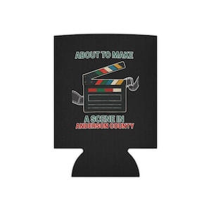 Peut inclure: Refroidisseur de canette noir avec un graphisme de clap de cinéma. Le clap a un dessus coloré et est entouré de bandes de film. Le texte sur le refroidisseur se lit "ABOUT TO MAKE A SCENE IN ANDERSON COUNTY."