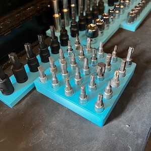 May include: A collection of metal sockets and bits, organized on light blue trays. The tools vary in size and shape, with a mix of silver and black finishes. The arrangement suggests a focus on organization and accessibility for mechanical work.