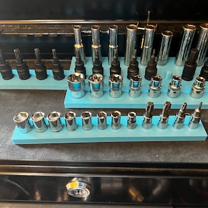 Può includere: Una collezione di varie bussole e inserti metallici, organizzati su supporti azzurri. Gli utensili sono disposti in file, con una varietà di dimensioni e forme, suggerendo un set completo per lavori meccanici.