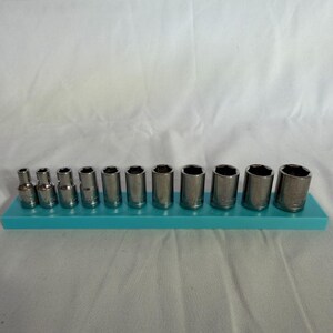 Könnte beinhalten: Ein Set aus zwölf silberfarbenen Metall-Steckschlüsseleinsätzen, die nach Größe aufsteigend auf einer rechteckigen, türkisfarbenen Kunststoff-Aufbewahrungsschiene angeordnet sind. Jeder zylindrische Einsatz hat eine Sechskantöffnung.