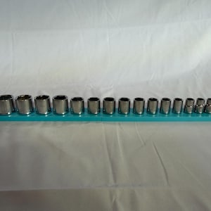 Könnte beinhalten: Ein Set aus sechzehn silberfarbenen Metall-Steckschlüsseleinsätzen, die in einer Reihe auf einer langen, rechteckigen Aufbewahrungsschiene aus hellblauem Kunststoff angeordnet sind. Die Einsätze variieren in der Größe, von groß nach klein.