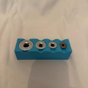 Könnte beinhalten: Ein hellblauer, rechteckiger Halter mit vier kreisförmigen Aussparungen, die jeweils einen silbernen Metall-Steckschlüsseladapter enthalten. Die Adapter haben schwarze Zentren und eingravierte Texte wie "Ratchet Socket Adapter".