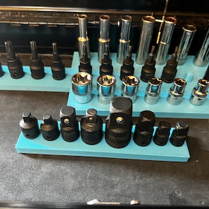 May include: A selection of sockets and bits, arranged on light blue holders. The tools are a mix of silver and black, including sockets, extensions, and bit holders. The tools are organised in a toolbox.