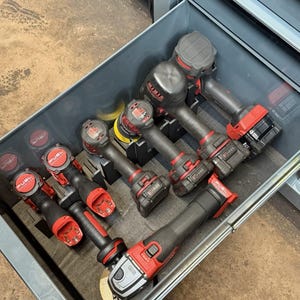 Pode incluir: Uma coleção de ferramentas elétricas sem fio Milwaukee M18 FUEL organizadas em uma gaveta de ferramentas de metal cinza. O conjunto inclui várias chaves de impacto, furadeiras e uma esmerilhadeira angular em preto e vermelho com baterias.