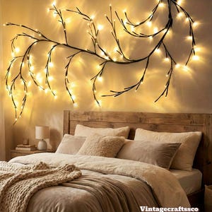May include: A bedroom scene featuring a wooden headboard, a bed with beige bedding, and a decorative branch with warm white fairy lights on the wall. A small lamp sits on a nightstand.