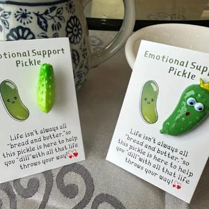 May include: Two cards with the text "Emotional Support Pickle" and a cartoon pickle illustration. One card has a 3D green pickle charm. The text reads, "Life isn't always all 'bread and butter,' so this pickle is here to help you 'dill' with all that life throws your way!"