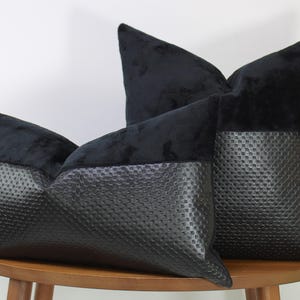 Könnte beinhalten: Drei schwarze Zierkissen mit zweifarbigem Design. Der obere Teil ist aus weichem, dunklem Samt und der untere Teil aus strukturiertem Kunstleder. Die Kissen sind auf einem runden Holztisch angeordnet.