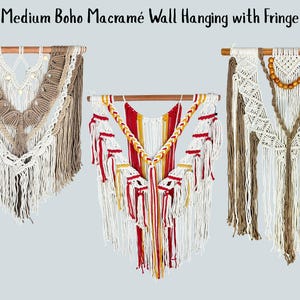 May include: Three macramé wall hangings suspended from wooden dowels. The left piece features tan and cream cord with beads. The center piece displays red, yellow, and white cord with braided details. The right piece uses cream and tan cord with wooden beads.