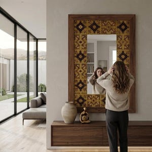 Puede incluir: Un espejo de pared rectangular con marco de madera oscura y un borde ancho decorado con un patr&oacute;n geom&eacute;trico repetitivo en tonos amarillo mostaza, marr&oacute;n y negro. El espejo est&aacute; montado sobre una mesa consola flotante de madera oscura.