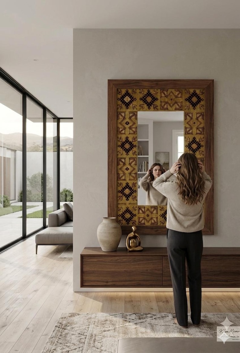 Puede incluir: Un espejo de pared rectangular con marco de madera oscura y un borde ancho decorado con un patr&oacute;n geom&eacute;trico repetitivo en tonos amarillo mostaza, marr&oacute;n y negro. El espejo est&aacute; montado sobre una mesa consola flotante de madera oscura.
