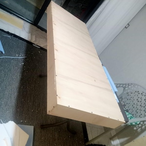 Puede incluir: Un estante o tablero de mesa rectangular de madera clara que presenta una superficie lisa y plana con patrones de veta visibles. Los bordes est&aacute;n construidos con paneles de madera delgados asegurados por peque&ntilde;os clavos met&aacute;licos espaciados.