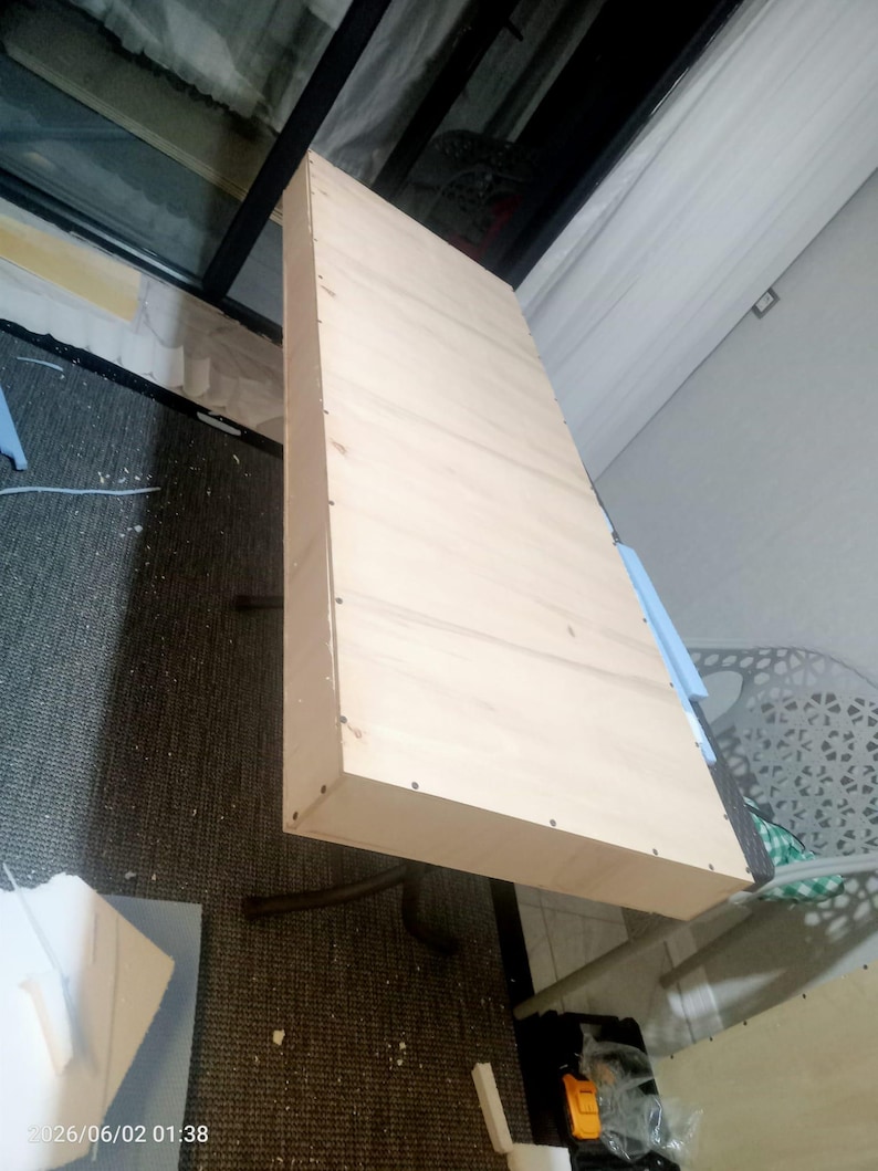 Puede incluir: Un estante o tablero de mesa rectangular de madera clara que presenta una superficie lisa y plana con patrones de veta visibles. Los bordes est&aacute;n construidos con paneles de madera delgados asegurados por peque&ntilde;os clavos met&aacute;licos espaciados.
