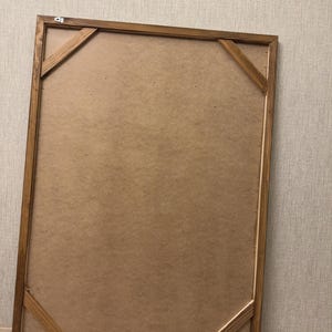 Puede incluir: Un marco de fotos rectangular de madera visto desde atr&aacute;s, con un acabado te&ntilde;ido en marr&oacute;n claro, un panel trasero de fibra y cuatro refuerzos diagonales en las esquinas. Los herrajes met&aacute;licos para colgar est&aacute;n fijados en los bordes.
