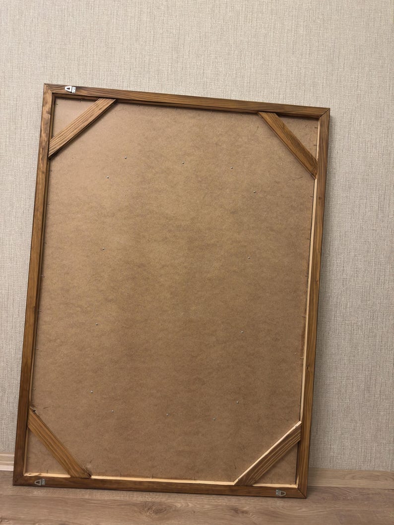 Puede incluir: Un marco de fotos rectangular de madera visto desde atr&aacute;s, con un acabado te&ntilde;ido en marr&oacute;n claro, un panel trasero de fibra y cuatro refuerzos diagonales en las esquinas. Los herrajes met&aacute;licos para colgar est&aacute;n fijados en los bordes.