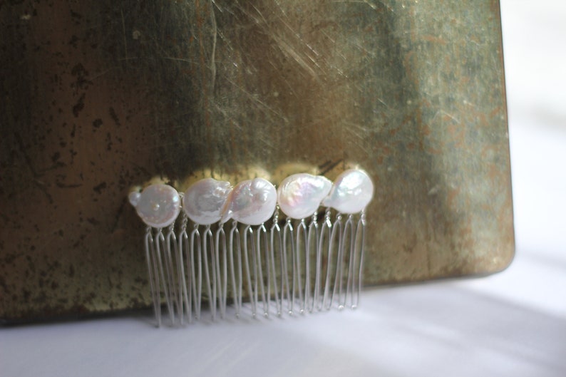 May include: A silver hair comb with five white pearl-like embellishments.