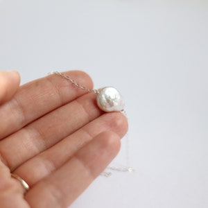 May include: A delicate silver chain necklace with a single, large, white baroque pearl pendant.