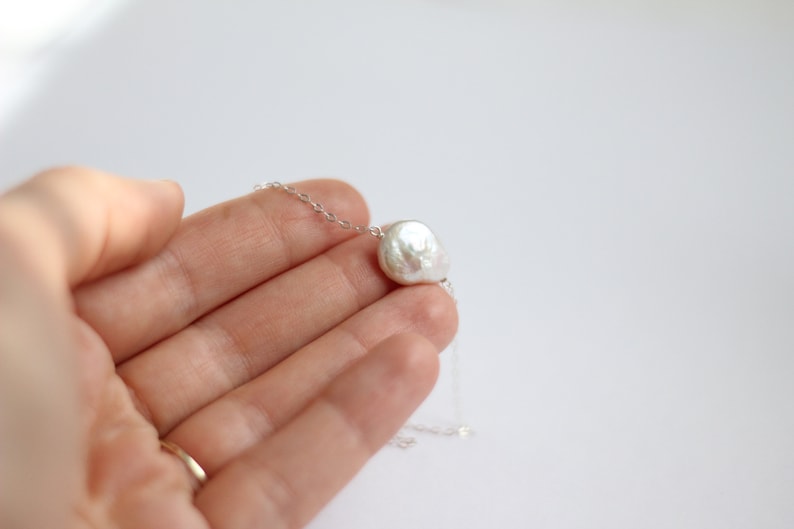 May include: A delicate silver chain necklace with a single, large, white baroque pearl pendant.