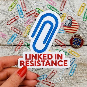May include: A sticker with the text "LINKED IN RESISTANCE" and a blue paperclip design. The image also includes colorful paperclips, a pin with an American flag, and a pin with text in a circle.