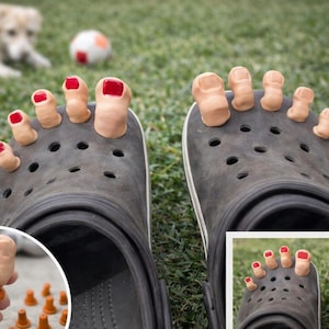 May include: A pair of black Crocs shoes with attached toe-shaped accessories. The toes are painted with red nail polish. A dog and a soccer ball are in the background on a grassy surface.