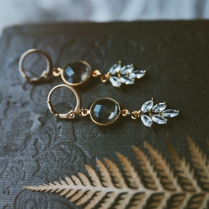 May include: A pair of gold earrings with a dark gray gemstone and a cluster of clear rhinestones.