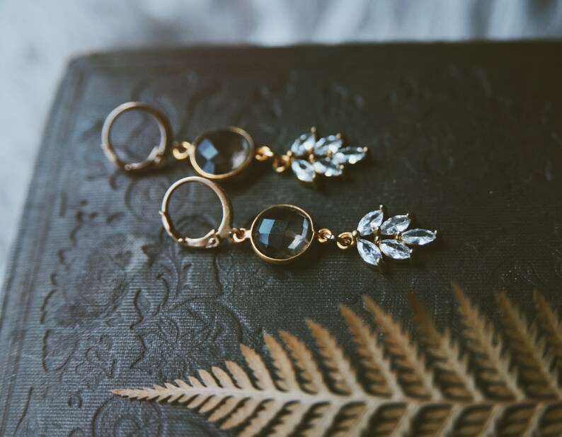 May include: A pair of gold earrings with a dark gray gemstone and a cluster of clear rhinestones.