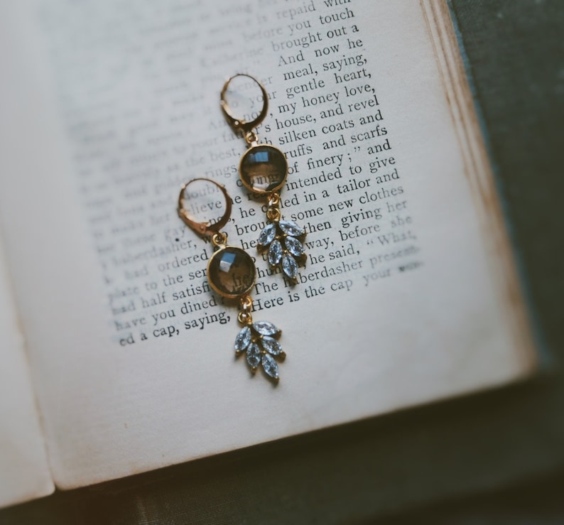 May include: A pair of gold earrings with a teardrop-shaped, clear glass stone and a dangling cluster of clear crystals.