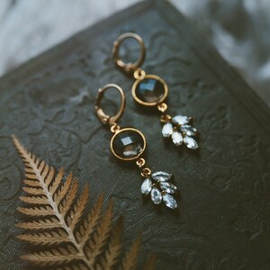 May include: A pair of gold earrings with black and clear crystal stones. The earrings have a delicate, leaf-like design.