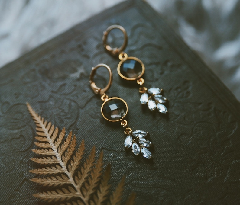 May include: A pair of gold earrings with black and clear crystal stones. The earrings have a delicate, leaf-like design.