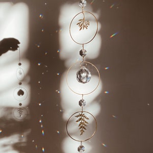 May include: A gold metal hanging mobile with crystal prisms and leaf cutouts. The mobile is hanging from a chain and is suspended from a ceiling.