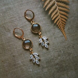 May include: A pair of gold earrings with clear crystal accents and brown gemstone drops. The earrings have a delicate, feminine design.