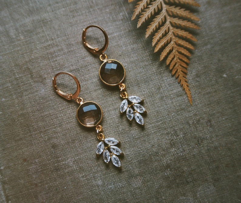 May include: A pair of gold earrings with clear crystal accents and brown gemstone drops. The earrings have a delicate, feminine design.