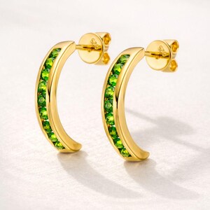 Pu&ograve; includere: Un paio di orecchini a forma di mezzaluna color oro. Ogni orecchino &egrave; foderato con piccole gemme verdi vibranti. Gli orecchini hanno una chiusura a perno e farfalla. Lo sfondo &egrave; di un morbido bianco sporco.