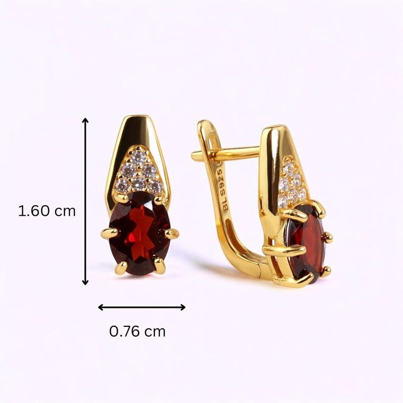 May include: Gold-tone earrings with a red oval gemstone and small clear stones. The earrings are 1.60 cm long and 0.76 cm wide. The earrings have a lever back closure.