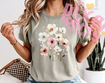 May include: Sage green t-shirt featuring a watercolor floral design. The design includes white and pink flowers with yellow centers and green stems. The shirt has rolled-up sleeves and a relaxed fit.