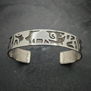 May include: A silver bracelet with a cutout design of an animal, possibly a bull or a bison, with intricate details. The bracelet has a smooth, polished finish.
