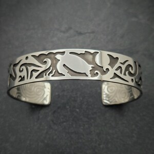 May include: Silver bracelet with a cutout design of a turtle and other sea life. The bracelet is open and has a smooth, polished finish.