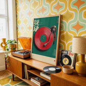 May include: A framed vertical poster featuring a graphic illustration of a red vinyl record on a turntable against a dark green background with Japanese text. The poster is displayed on a wooden sideboard next to a record player and an ABBA record.
