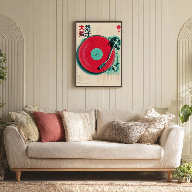 Op de afbeelding: Een ingelijste poster met een rode vinylplaat op een platenspeler, met Japanse tekst linksboven. De poster heeft een cr&egrave;mekleurige achtergrond en wordt weergegeven boven een beige bank met decoratieve kussens.