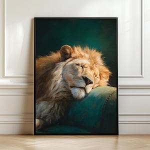 Op de afbeelding: Een ingelijste kunstdruk met een slapende leeuw. De leeuw heeft een gouden manen en rust zijn hoofd op een turquoise kussen. De achtergrond is donkergroen en de lijst is zwart.