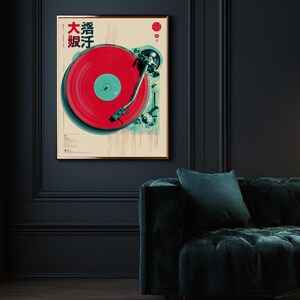 Op de afbeelding: Een ingelijste poster met een vintage platenspeler ontwerp. Het kunstwerk toont een rode vinylplaat met een turquoise middelpunt, tegen een cr&egrave;mekleurige achtergrond. Japanse tekst is zichtbaar bovenaan. De lijst is goudkleurig.