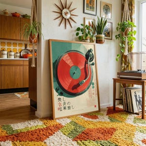 May include: A framed poster featuring a graphic illustration of a turntable with a vibrant red vinyl record. The artwork includes Japanese text characters and a dark green background, presented in a simple wooden frame leaning against a white wall.